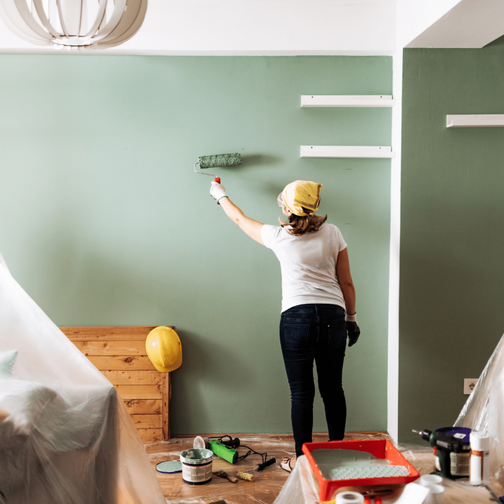A woman doing home renovations and painting the living room wall.