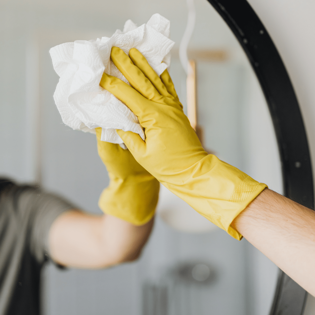 A man that is wearing gloves cleaning a round mirror.