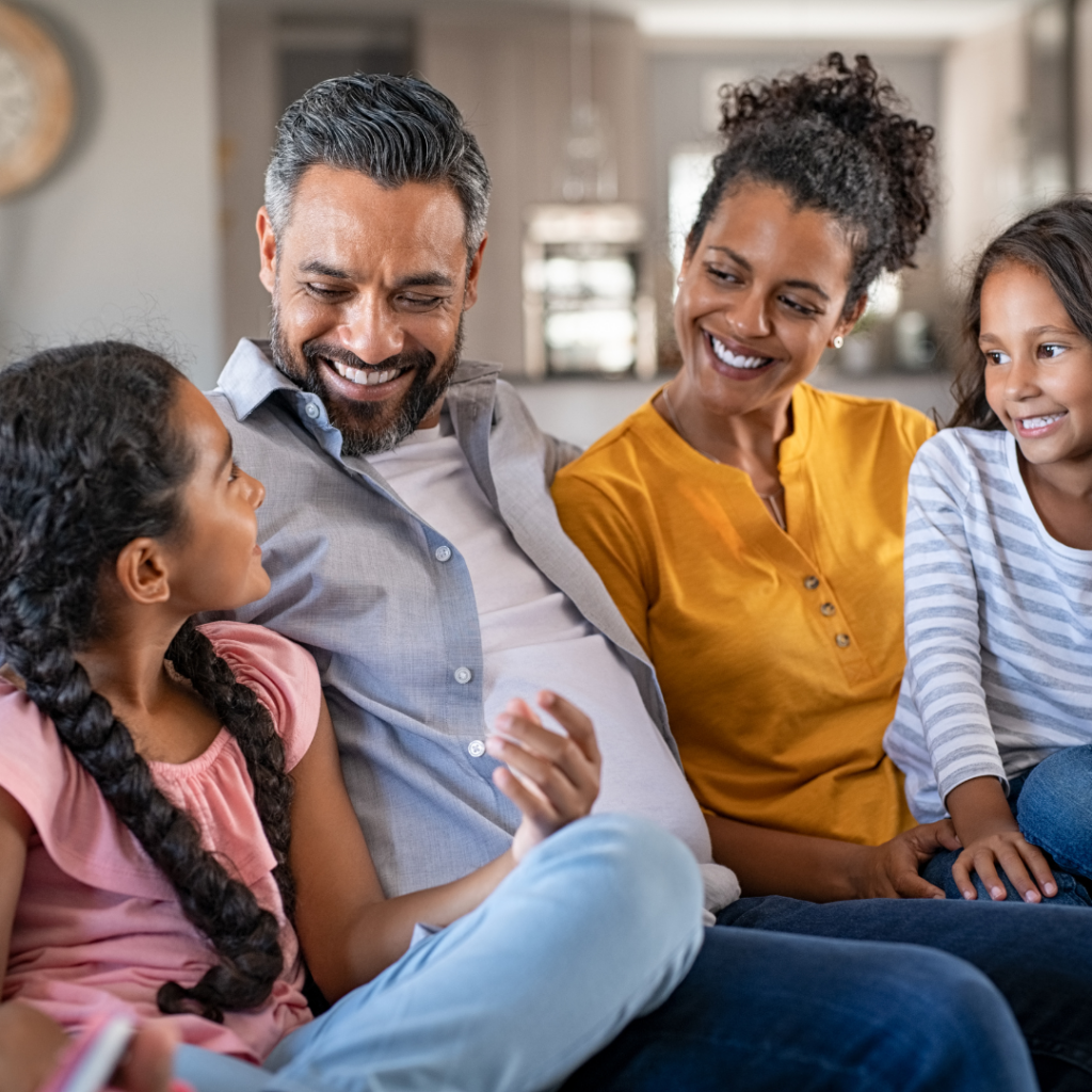 A family of four sitting on the couch laughing together.