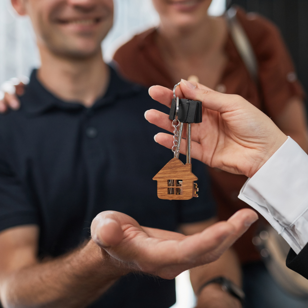 A happy couple smiling as the real estate agent hands them the keys to their new house.