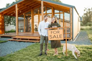 Happy couple standing outside of home near a for sale sign.