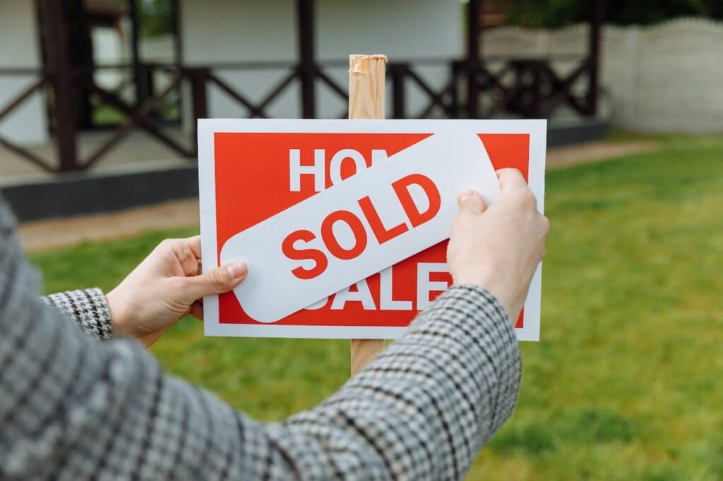 A person sticking a sold sign on top of a for sale sign.