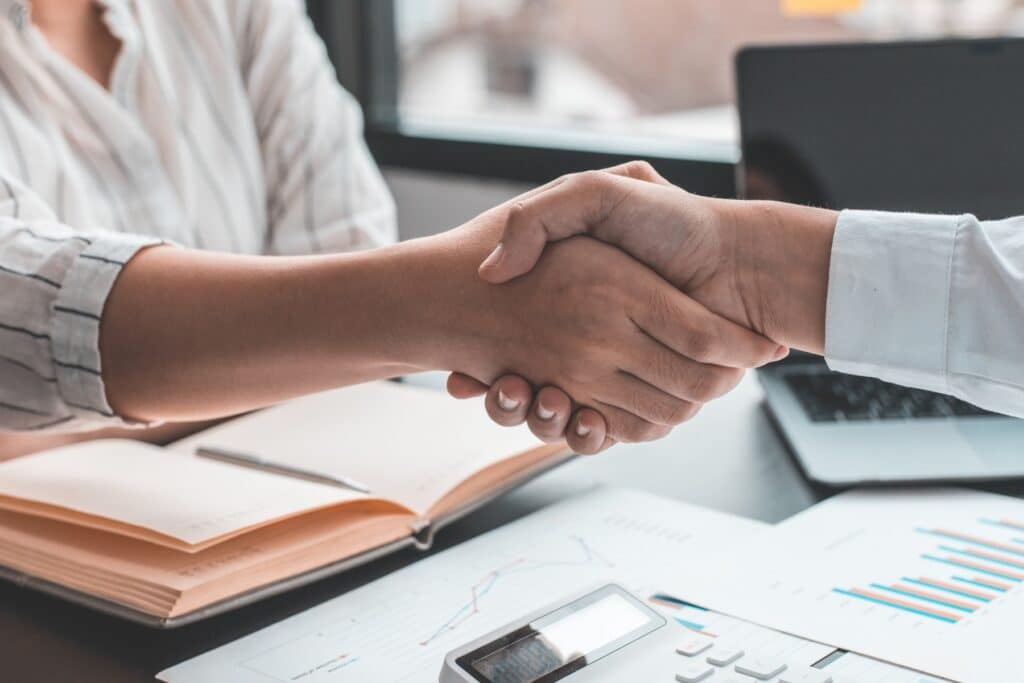 Two people sitting at a desk and shaking hands.