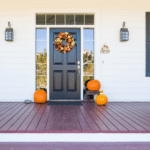 A spacious porch with a front door that is beautifully decorated with fall decor.