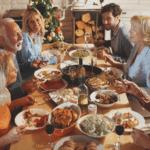 Family and friends talking and eating Thanksgiving dinner at a large wooden table.