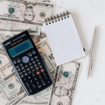 A calculator, notepad, and money on a desk.
